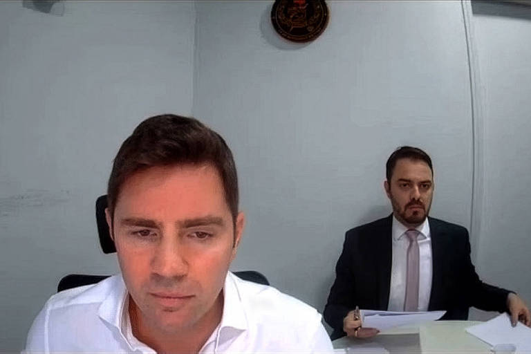 Vorcaro durante depoimento por vídeo à Polícia Federal em 28 de agosto em uma sala na Papudinha; ao fundo, o advogado Thiago Machado - Reprodução - 28.ago.2026/Uol